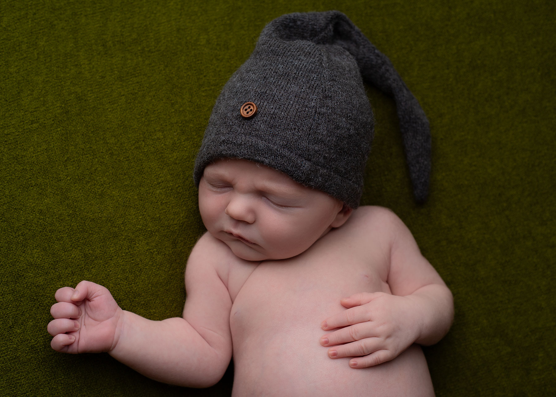 Newborn baby resting comfortably on a dark green blanket