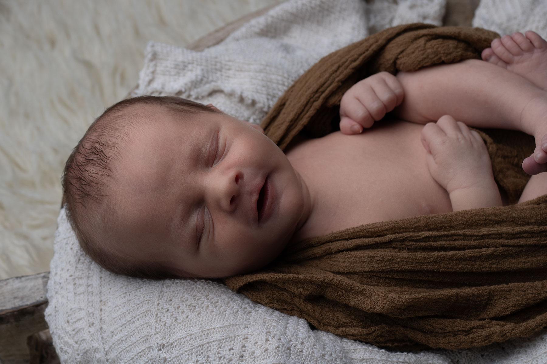 Newborn baby smiling whilst wrapped in a brown blanket