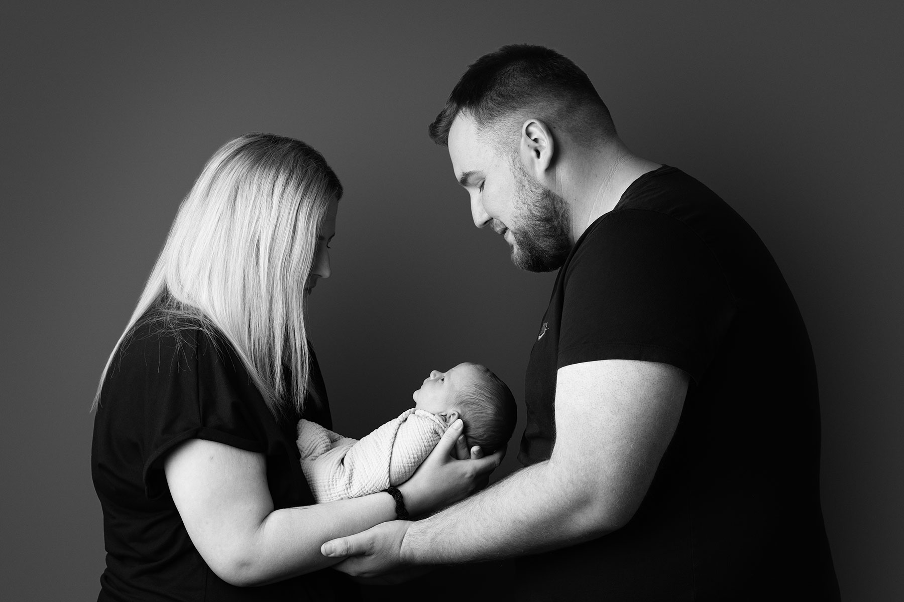Black and white portrait of a mother and father holding their newborn