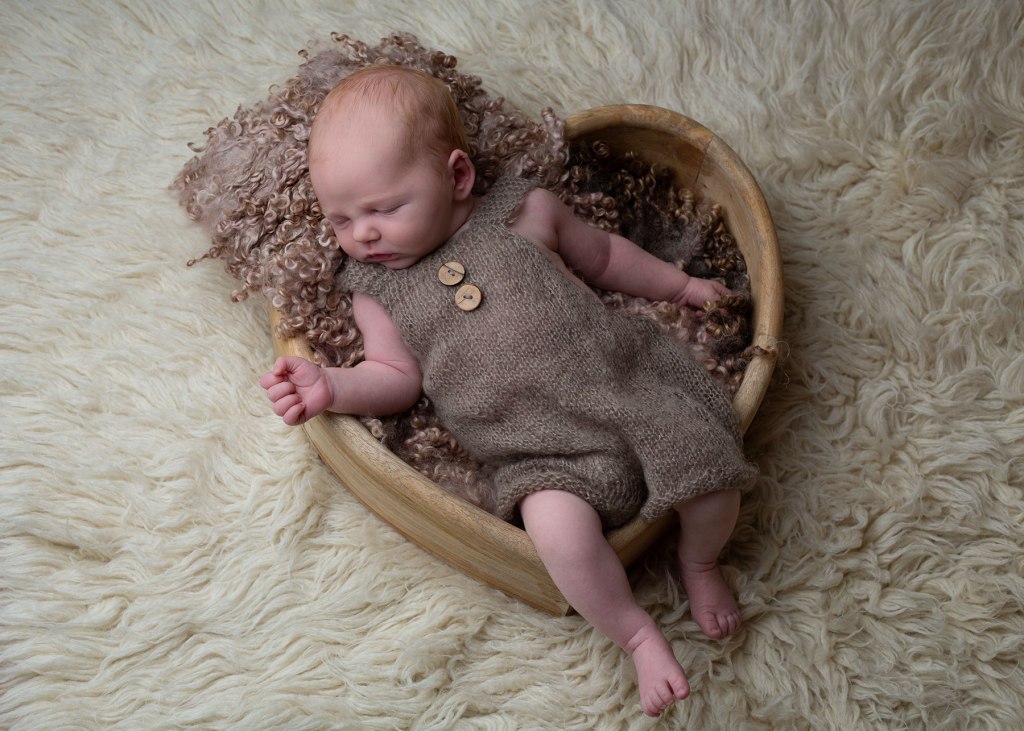 Newborn baby wearing a knitted outfit, whilst sleeping in a wooden heart prop. Captured during an in-home newborn photoshoot in Ceredigion