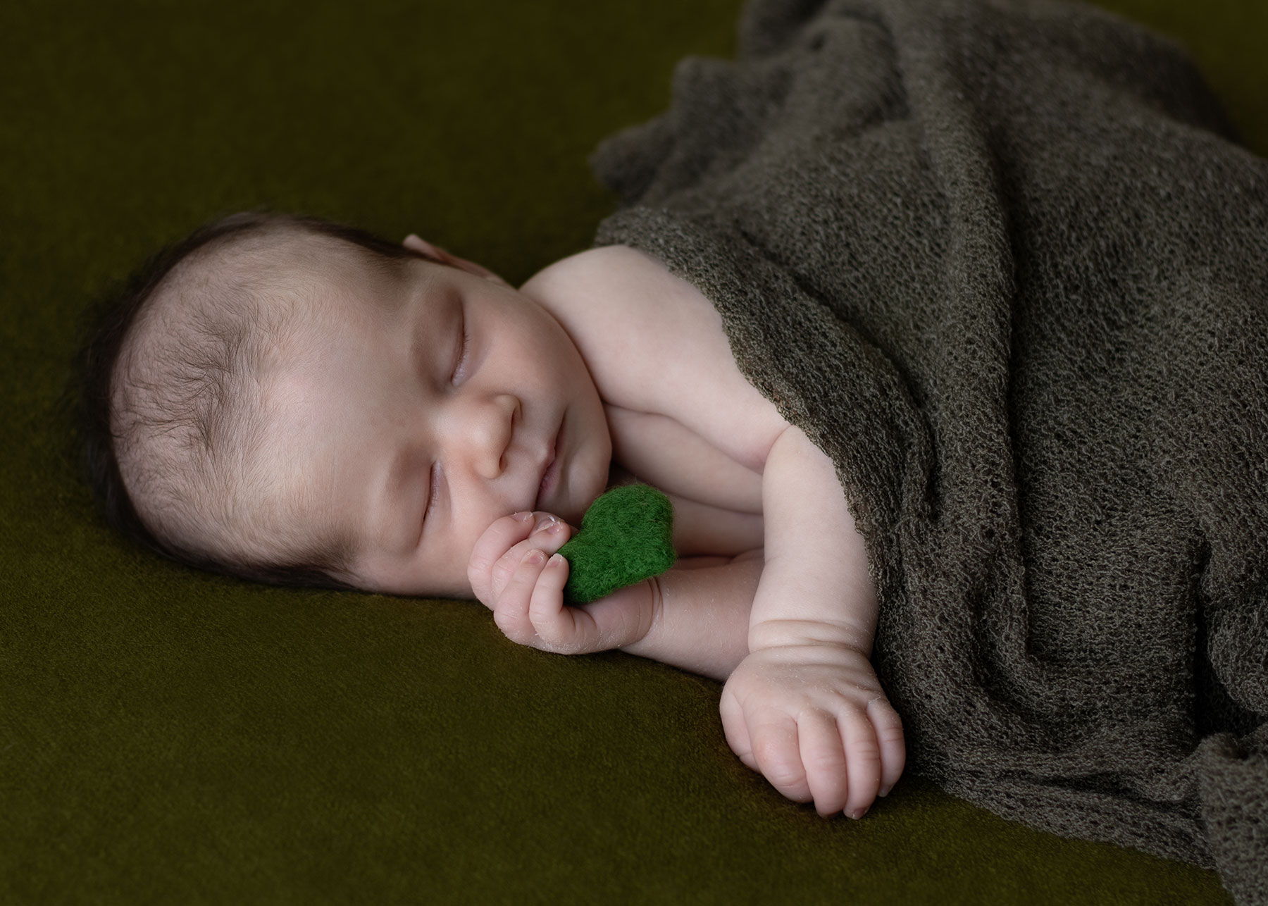 Newborn baby boy holding a green felted heart during an in-home newborn photoshoot