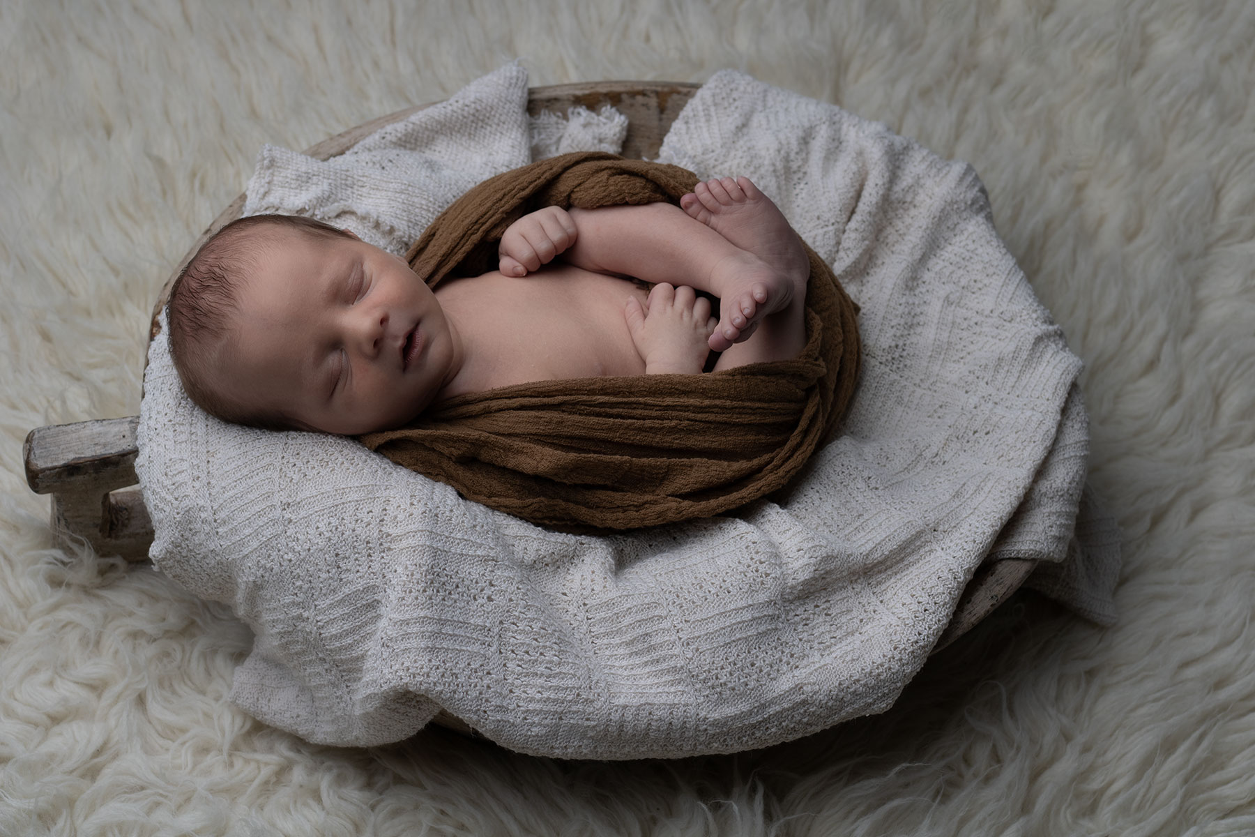 Newborn baby sleeping peacefully in a wooden bowl with a newborn photographer in Ceredigion