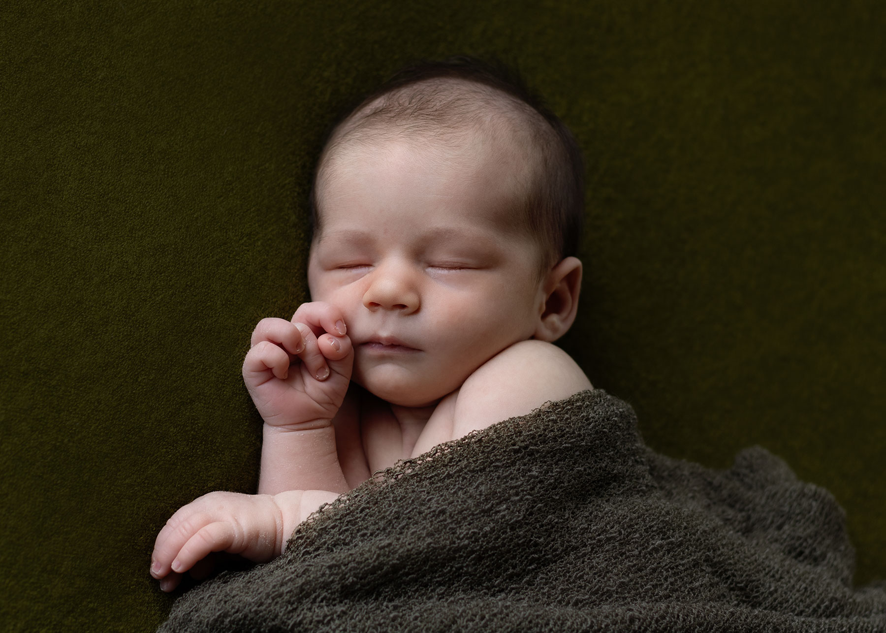 Baby boy wrapped in a green blanket during relaxed newborn photoshoot