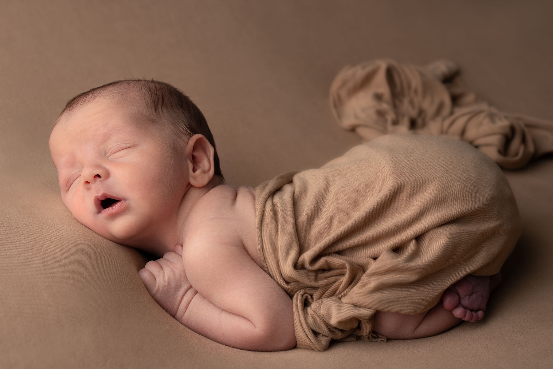 Newborn baby wrapped in a soft, brown blanket at home